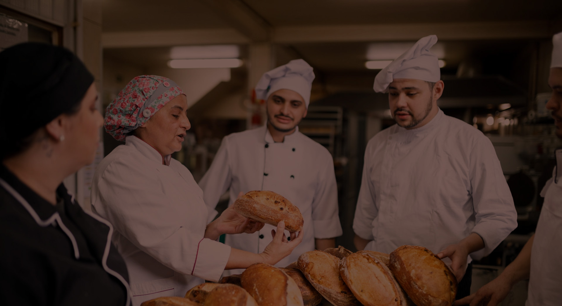 A group of professional bakers stand together in their white chef gear, examining artisanal sourdough loaves.