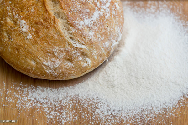 A close-up of a floured wooden table and a round loaf of artisanal bread.