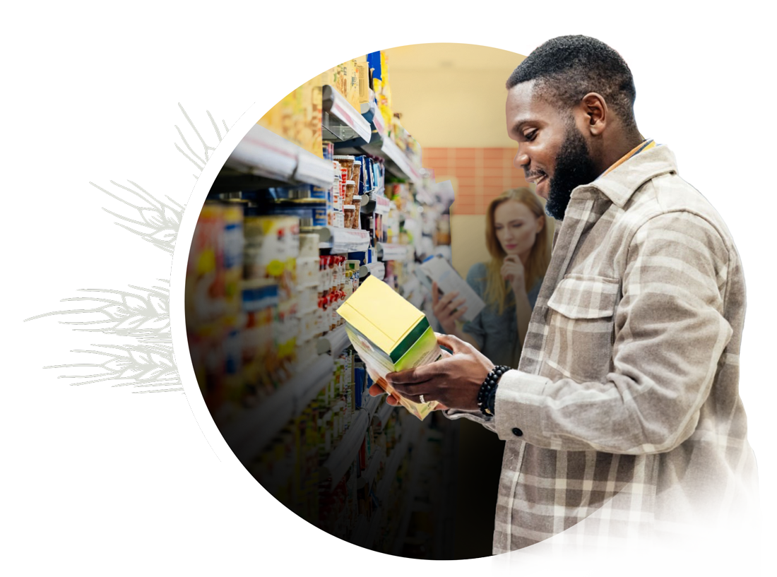 A man stands in a supermarket aisle, reading the writing on a package.