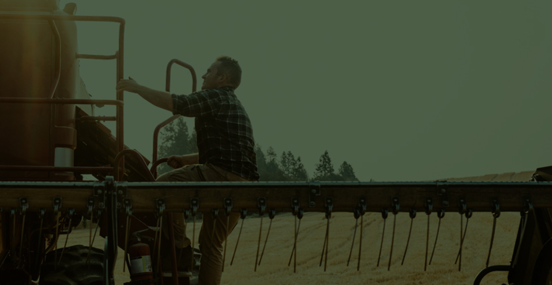 A farmer climbs up the side of his combine harvester. He is outdoors, in the wide open prairie.