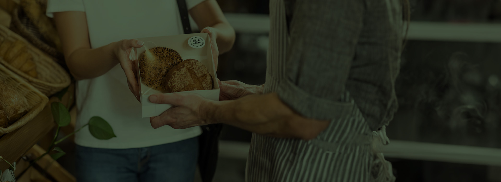 A bakery employee hands a package with the Ecolabel Winter Wheat label on it to a customer. The package contains two lovely rolls of bread.